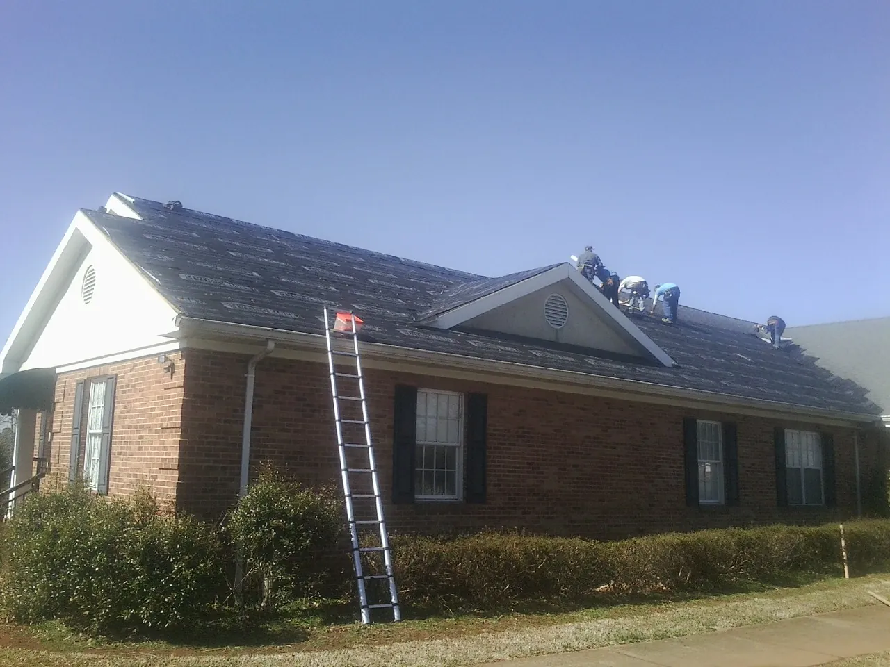Crew tearing shingles off a brick ranch roof with a ladder set — Metal Roof Repair work by our crew in Palmetto